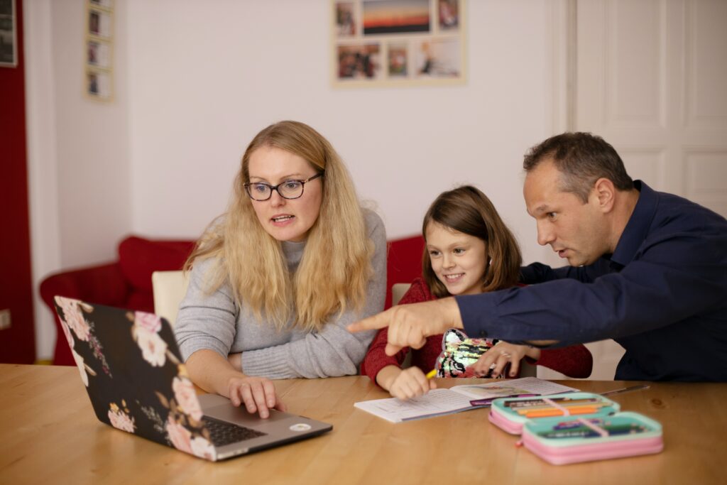 Two parents helping their child with a laptop.